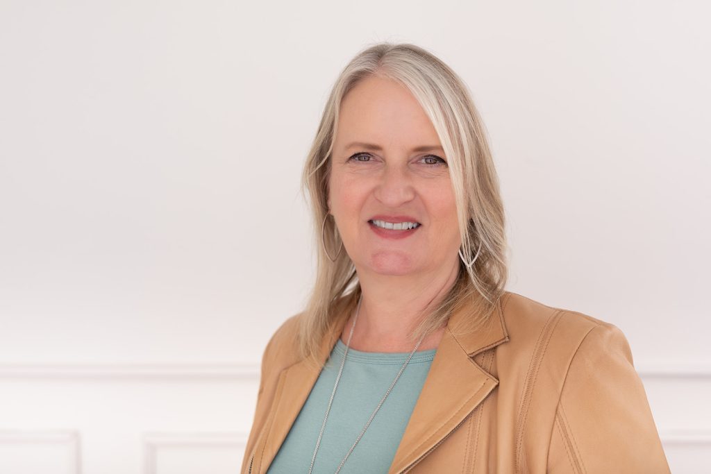 Professional headshot of Patti Sanchez, experienced B2B communication strategist and corporate storytelling expert. She is wearing a beige blazer and an aqua green top and smiling warmly at the camera.